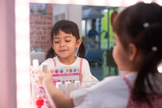 Happy young girl playing with toy makeup in front of a mirror, exploring beauty roleplay and creative self-expression while developing imagination, confidence, independence, and social learning skills