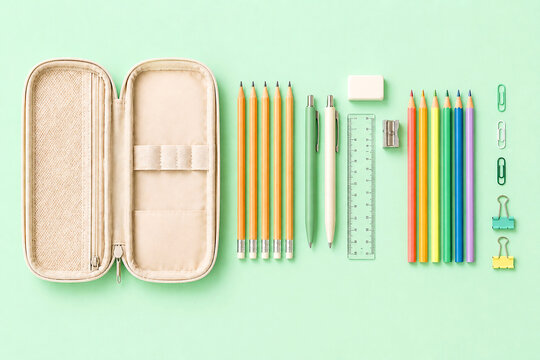 Pencil case with stationery on green background. Office supplies and school equipment organized in flat lay. Educational tools for student study, creative drawing and writing work.