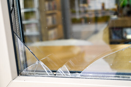 Broken window glass with sharp cracks in a modern building frame.Close-up of a shattered glass windowpane with large cracks and sharp edges in a modern plastic frame. Concept of vandalism, property da