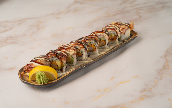 Gourmet tempura ebi sushi roll topped with unagi and sauce drizzle served on an elongated ceramic platter