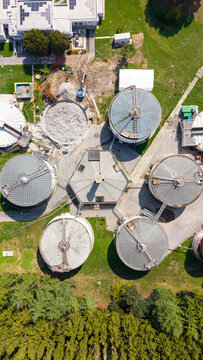 Aerial view of an anaerobic digestion water plant featuring large circular treatment tanks, a central hexagonal building, and surrounding green space in Milan, Lombardy, Italy.