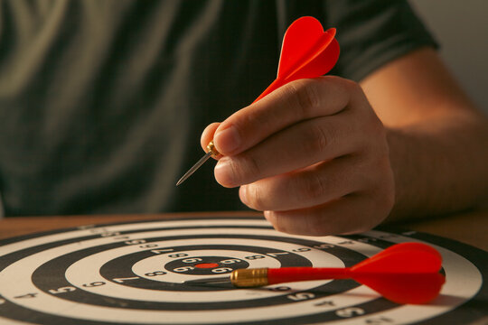 Man's hand is aiming at the target with red dart arrow.