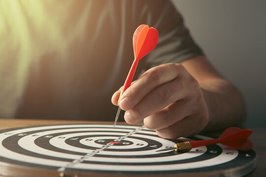 Man's hand is aiming at the target with red dart arrow.