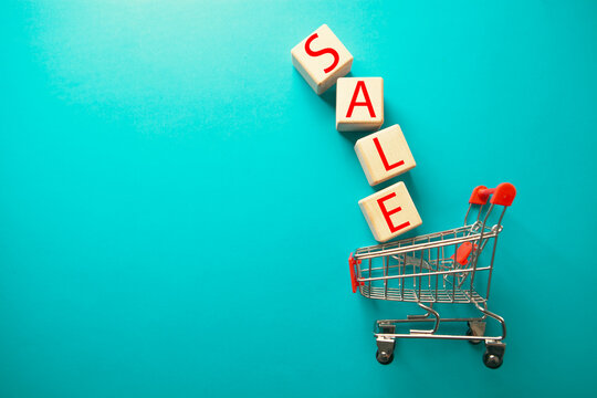 Word SALE made of wooden cubes and shopping cart on blue background