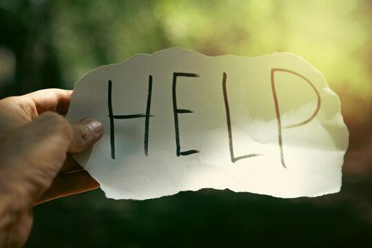 Help written on a piece of paper held by a man's hand