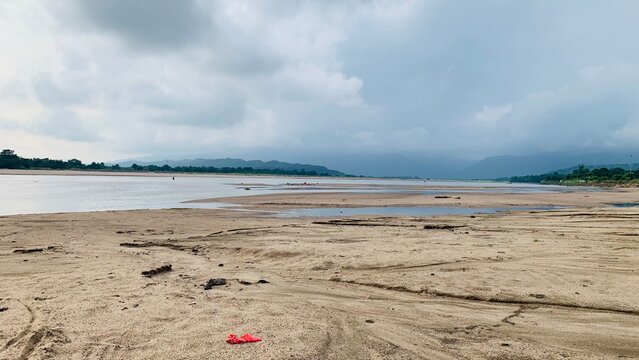 Wide sandy riverbank with calm water under a cloudy dramatic sky