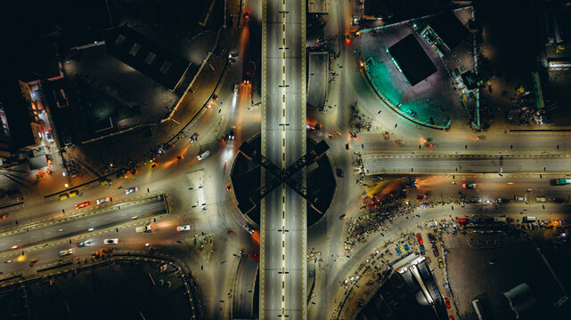 Aerial view of a busy roundabout and bridge intersection at night, with illuminated roads, moving vehicle light trails, and surrounding urban infrastructure in Kano, Kano, Nigeria.