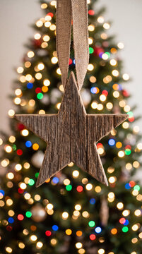Wooden star ornament hanging against a softly blurred background of festive holiday lights.