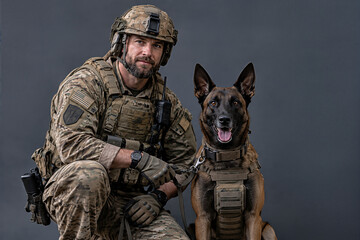 Fototapeta premium A soldier and his military working dog stand before a colored backdrop