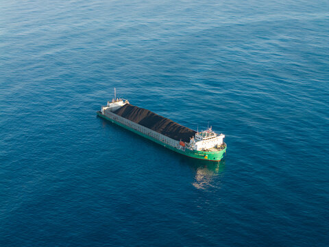 Aerial view of a large coal barge transporting a heavy load of coal across the deep blue ocean waters in Buleleng, Bali, Indonesia.