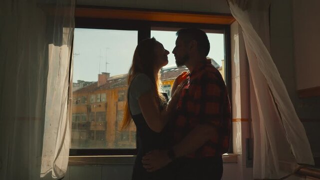Romantic couple kissing and embracing by a window