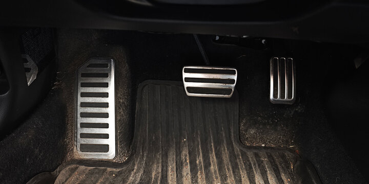 Driver's view of accelerator, brake and clutch pedals on a dark floor mat in a manual transmission car, close up interior detail