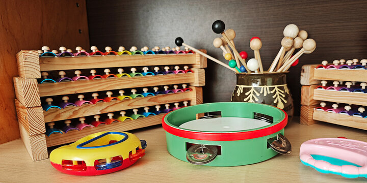 Assorted music making tools for kids, such as tambourines, maracas, and a set of wooden handbells, displayed neatly on a shelf