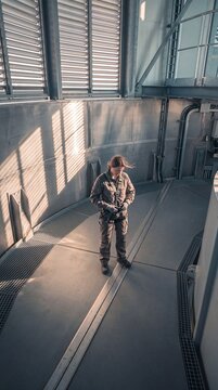 Female industrial engineer wearing protective workwear and safety harness prepares for maintenance work inside a modern technical facility