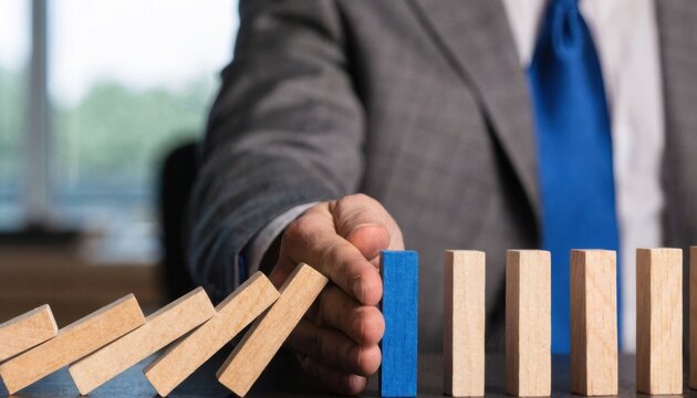 Businessman stopping falling dominoes with a blue block