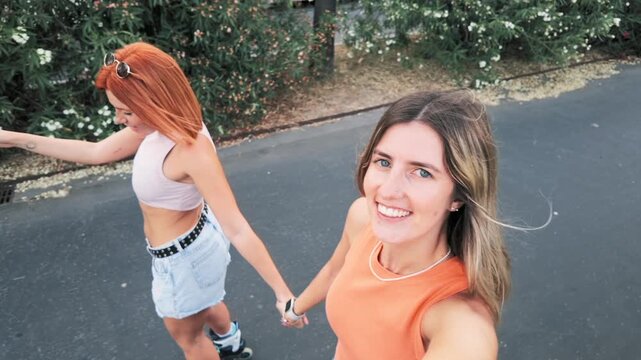 Happy girlfriends holding hands while inline skating outdoors
