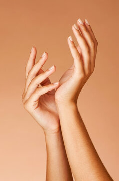 Close-up of elegant woman's hands with neat manicure gestures against a beige background.