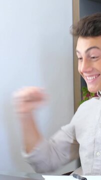 Overjoyed young businessman celebrating a professional achievement while working at his desk, showing a gesture of victory and success with a happy and surprised expression on his face