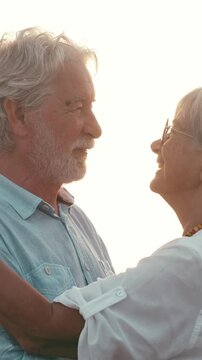 Happy senior caucasian couple enjoying their vacation, romantically dancing and hugging on the beach at sunset, smiling with love and affection during their golden years of retirement