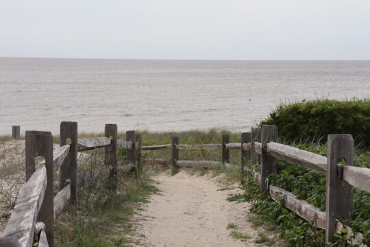 A footpath etched into the sand dunes, sloping down to a beachhead of the Cape May Bay on a quiet summer evening.