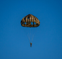 German Bundeswehr paratrooper descending under a round military parachute against a clear blue sky. © Frank