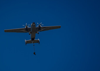 A German Bundeswehr paratrooper jumping from a military transport aircraft via static line against a clear blue sky © Frank