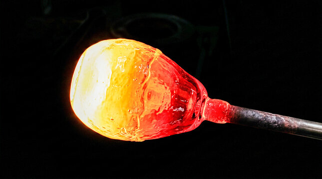 Molten hot glass glowing on a blowpipe during the traditional glassblowing process in a workshop.