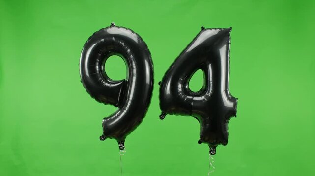 Black foil number ninety-four balloon floating up on green screen background
