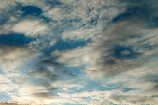 Blue sky with dramatic grey and white clouds at sunset, cloudscape background. Layered formations covering the frame with bright patches of light in a peaceful atmosphere