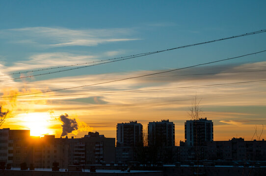 City sunset background. A bright sun setting behind residential buildings. Power lines crossing the sky above silhouetted rooftops and distant high rises