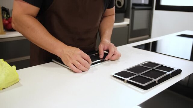 Man replacing the charcoal filter of a cooker hood on a white kitchen counter