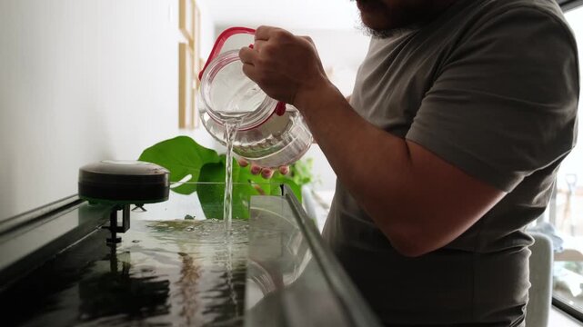 Person performing routine maintenance by adding clean water to a home fish tank