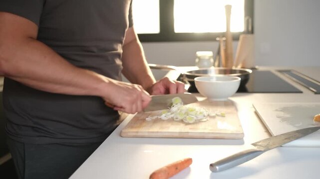 Male hands chopping vegetables with a knife in a modern kitchen with natural morning light