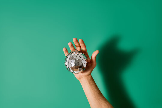 Hand Holding Shiny Silver Disco Ball Christmas Ornament Over Green Background