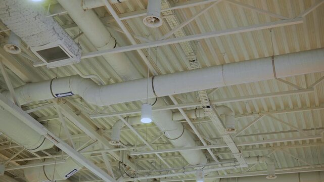 ceiling of a commercial building, featuring exposed industrial pipes and fluorescent lighting. It captures details such as the arrangement of the pipes and the layout of the lights