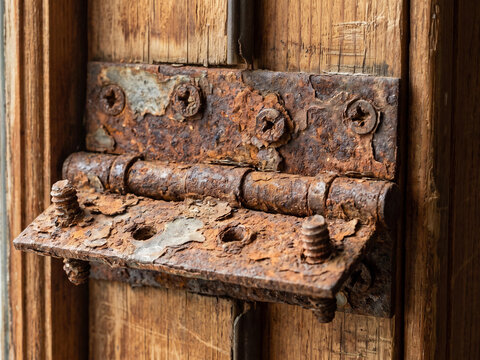 Rusted metal hinge attached to weathered wooden door frame with corrosion and flaking paint