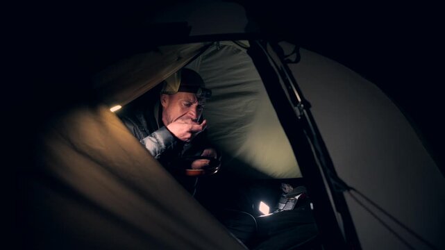 A man eating food in a tent at night