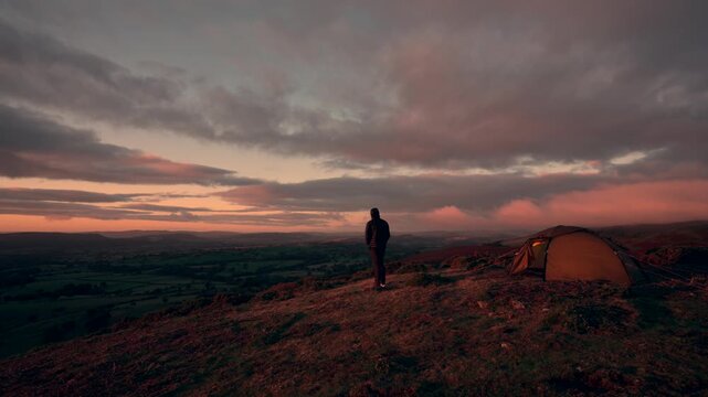 A man standing outside his camping tent on a hill in amazing sunrise weather