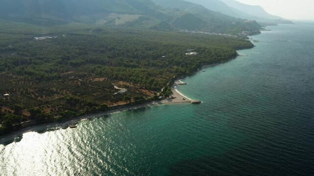 Oseka pebble beach extends into clear Adriatic Sea in Baska Voda on Makarska Riviera. Sparkling water and lush pine forest frame scenic coast for Mediterranean summer vacation in Croatia.