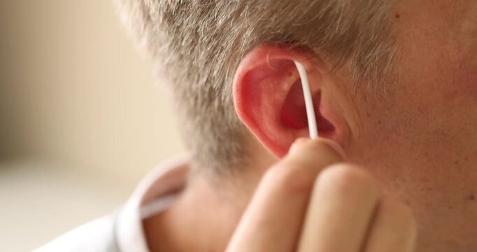 Man cleaning ear with cotton swab indoors, closeup