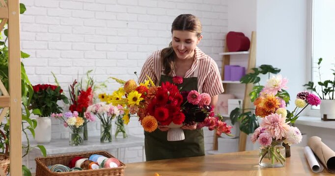 Florist making bouquet of beautiful dahlia flowers at wooden table in shop