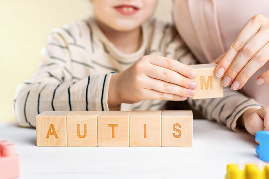 Mother and child arranging wooden alphabet blocks spelling autism together on a table, hands close up in family bonding and awareness concept.