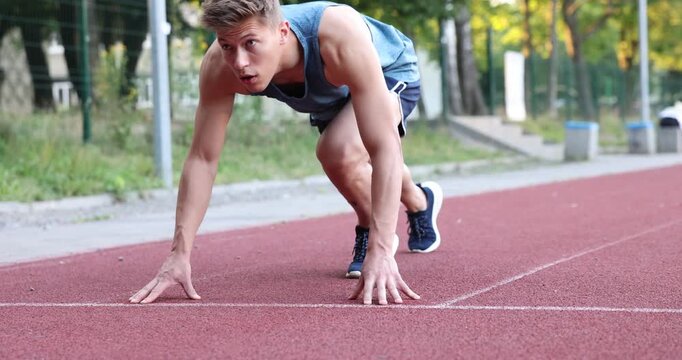 Athletic man getting into start position and running at stadium. Camera tilting and moving left