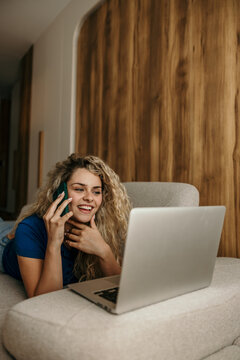 Woman making phone call on couch while working on laptop