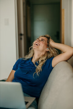 Happy woman laughing at home with laptop and earbuds