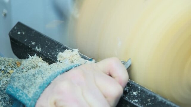 Woodturning on a wood turning lathe. Carpenter shaping a piece of wood into a bowl with a skew chisel, producing many wood curls. Design, art, carpentry, craftsmanship and manufacturing concept.	