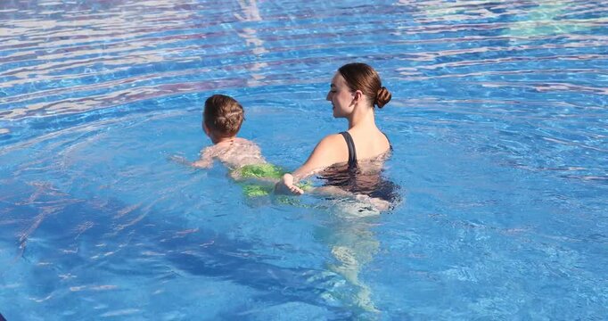 Swimming lesson. Coach teaching little boy to swim in pool. Camera moving backwards