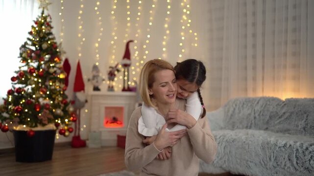 Young girl affectionately hugs her mother from behind in a christmas decorated living room