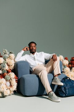 Stylish man seated on blue armchair surrounded by dried flowers for lifestyle branding background and elegant banner design