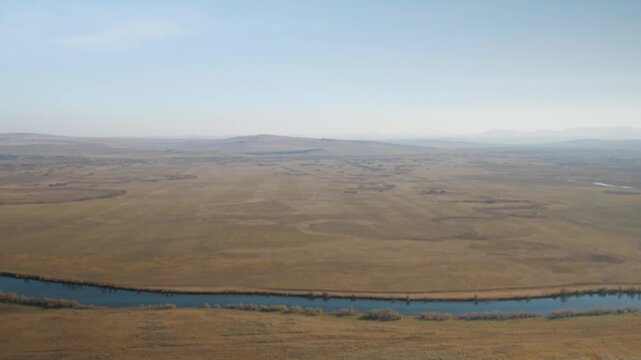 A handheld camera tilts up from rocky foreground to reveal a vast, yellowed autumn steppe and the winding Bely Iyus river. A scenic view of the wild, untouched landscape in Khakassia, Russia.